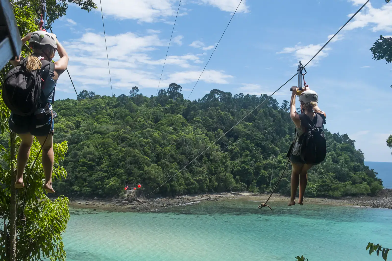 Zip-liners crossing a turquoise bay between the islands of Tunku Abdul Rahman Park