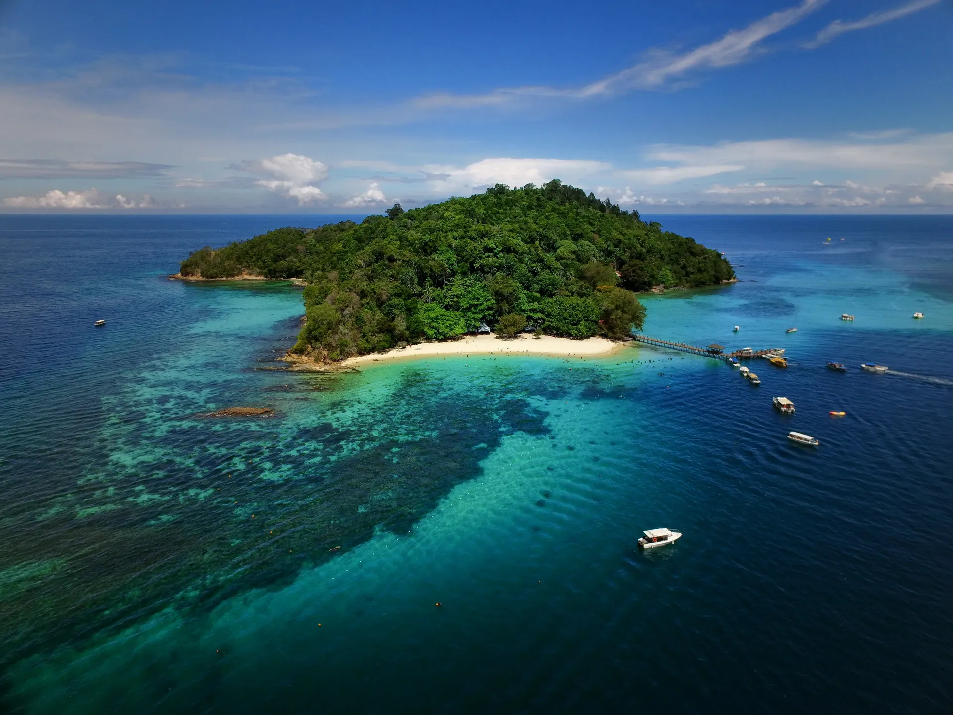 Aerial view of a forested island surrounded by coral reefs and turquoise water, Sabah